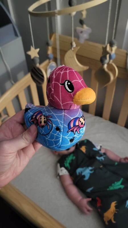 A plush duck with a spider web design in a nursery with hanging mobiles.