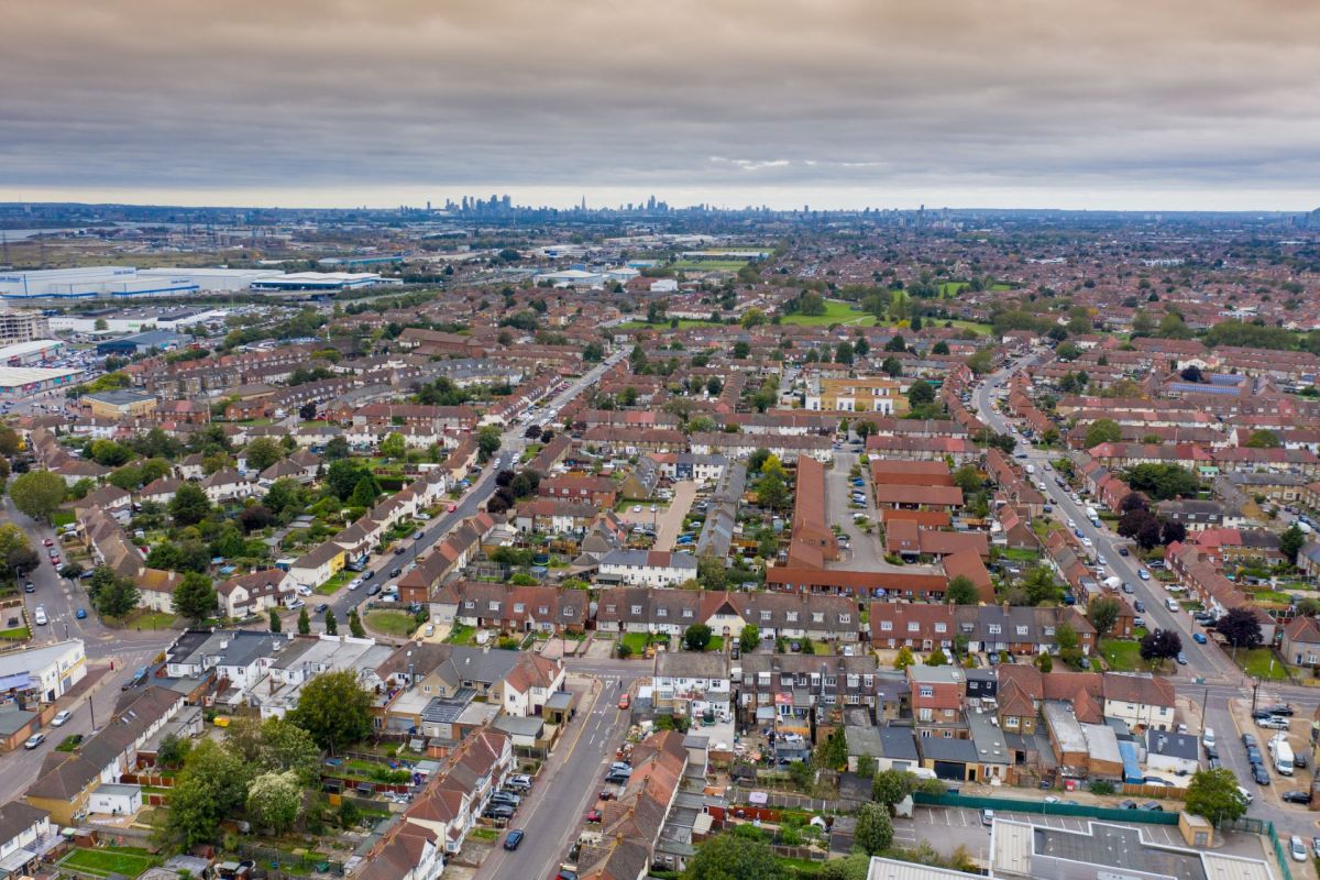 An aerial view of a suburban neighborhood with rows of houses and a distant skyline.