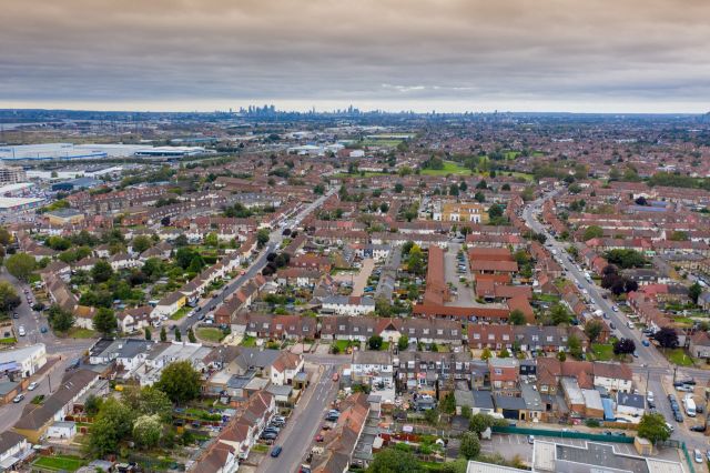 An aerial view of a suburban neighborhood with rows of houses and a distant skyline.