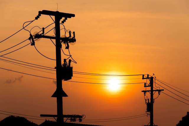 Silhouetted power lines and poles against a vibrant sunset sky.