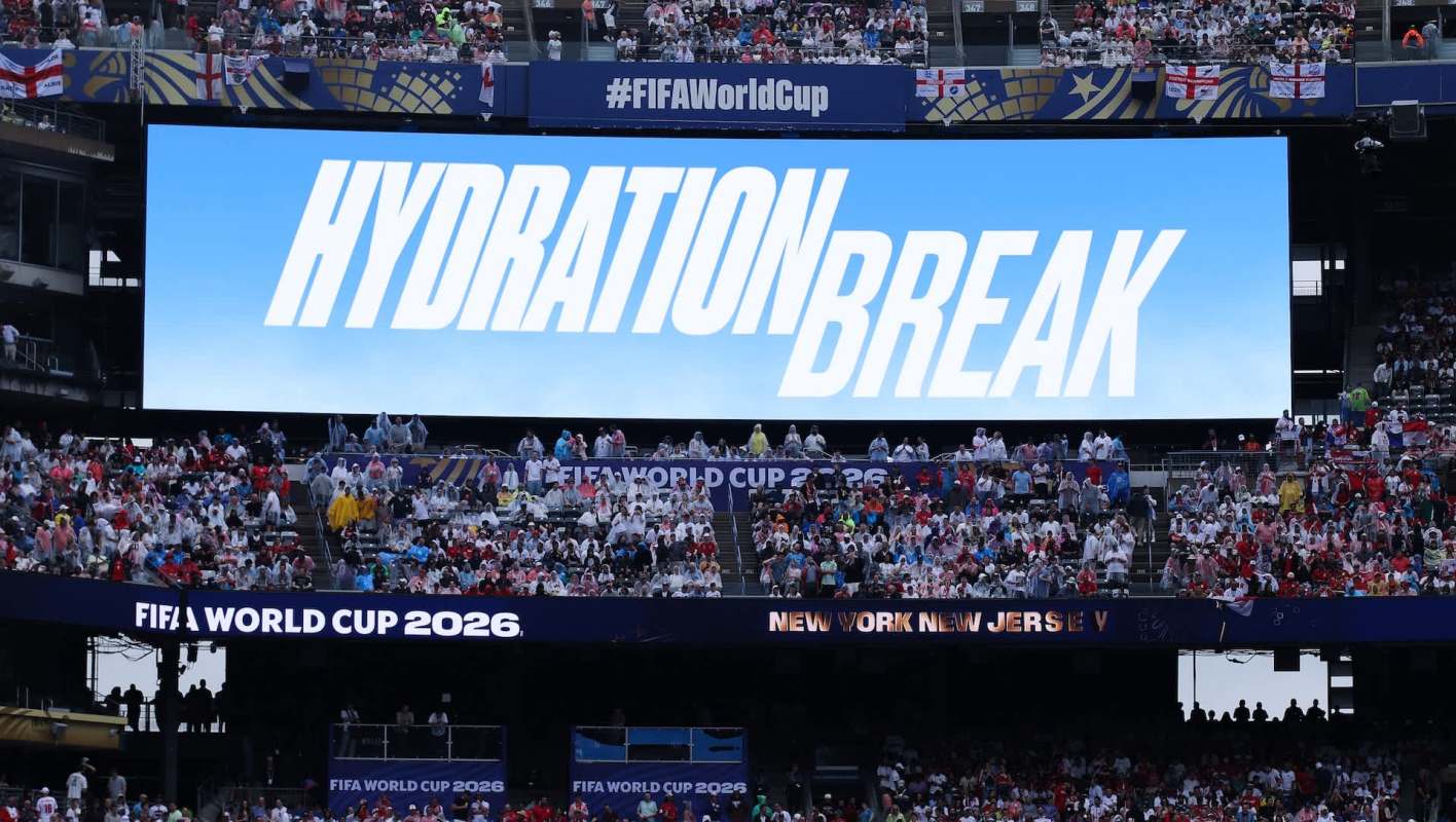 A large screen displays "HYDRATION BREAK" at a crowded FIFA World Cup stadium with fans in rain gear.
