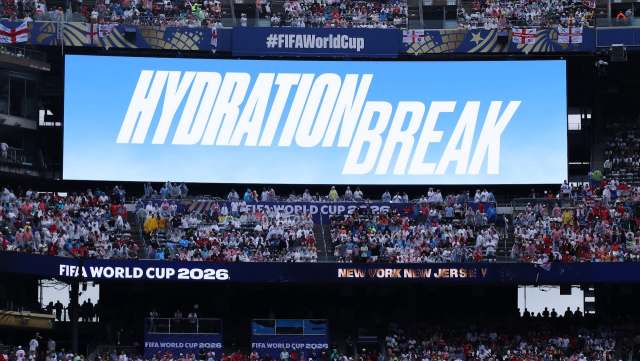 A large screen displays "HYDRATION BREAK" at a crowded FIFA World Cup stadium with fans in rain gear.
