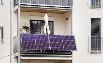 A balcony featuring solar panels, a white umbrella, and potted plants against an apartment building backdrop.