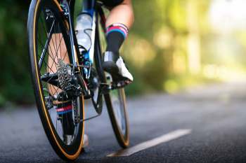 A close-up view of a cyclist's leg and bike wheel on a path surrounded by greenery.