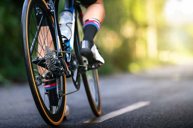 A close-up view of a cyclist's leg and bike wheel on a path surrounded by greenery.
