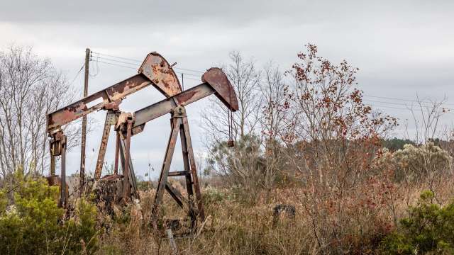 Two rusted oil pump jacks stand amid overgrown vegetation.