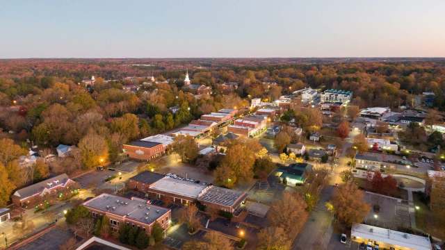 Aerial view of a small town during dusk, showcasing tree-lined streets and illuminated buildings.