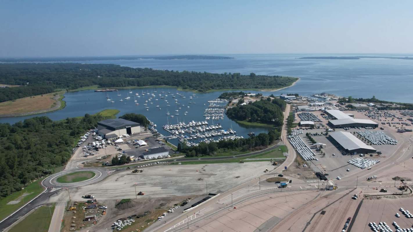 Aerial view of a marina surrounded by green land, with parked boats and vehicles visible.