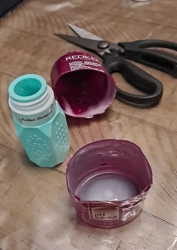 A close-up of a teal shampoo bottle being filled with creamy pink shampoo, set on a wooden surface.