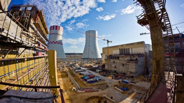 A construction site featuring large cooling towers and scaffolding against a blue sky with scattered clouds.