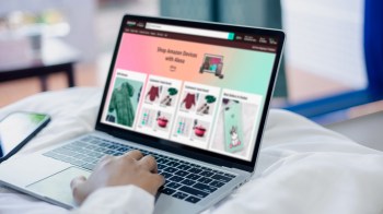 A person browsing an online shopping website on a laptop while sitting on a bed.