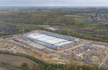 An aerial view of a large construction site with a warehouse and various machinery surrounded by autumn foliage.