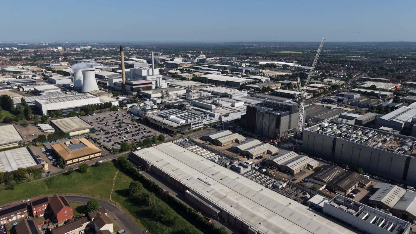 An aerial view of a sprawling industrial area with factories, parking lots, and a construction crane against a clear blue sky.