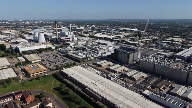 An aerial view of a sprawling industrial area with factories, parking lots, and a construction crane against a clear blue sky.