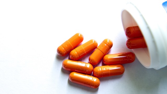 Orange capsules spill out of an open pill container.