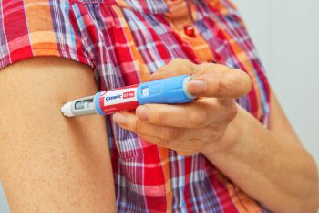 A woman administering an injection using an Ozempic pen on their upper arm.