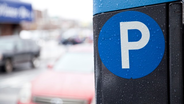 A close-up of a blue parking sign with the letter "P" on a rainy day, with blurred cars in the background.