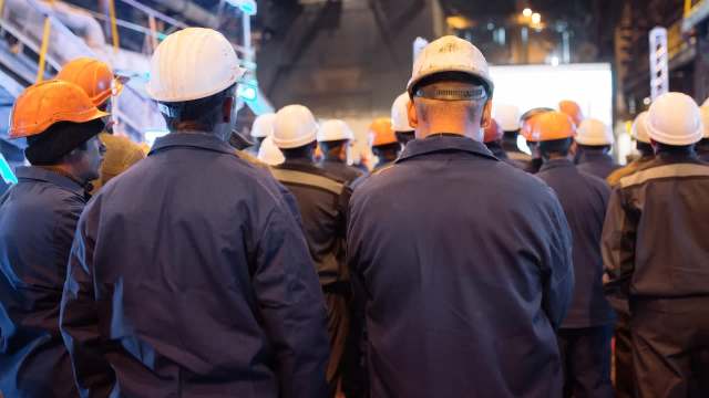 A group of workers in hard hats facing a large screen.