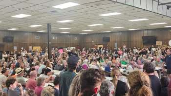A crowded community meeting with people holding protest signs.