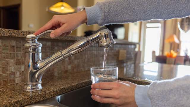A person fills a glass with water from a modern kitchen faucet.