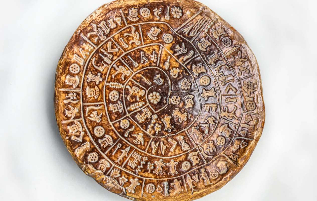 A round, ancient artifact with engraved symbols and figures arranged in concentric circles.