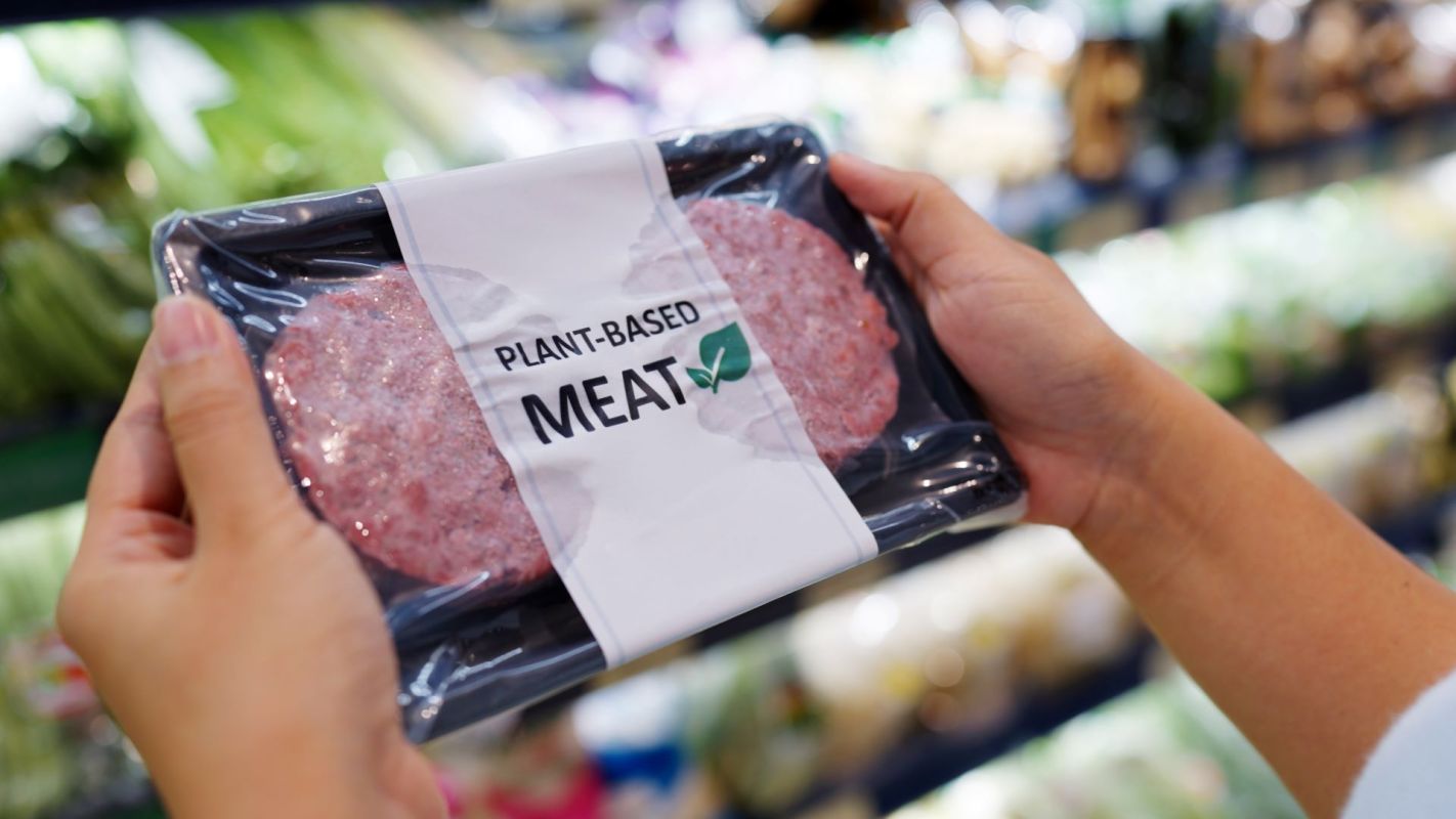 A person holding a package of plant-based meat in a grocery store.