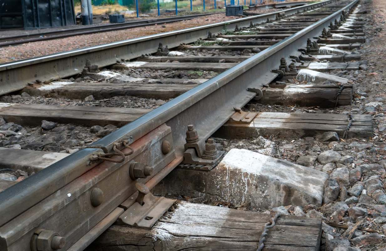 A close-up view of railway tracks with wooden ties and gravel, showing the track components and surroundings.