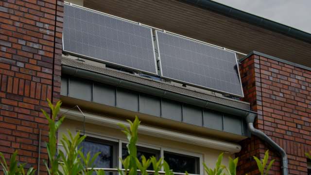 Two solar panels mounted on a balcony of a brick building.