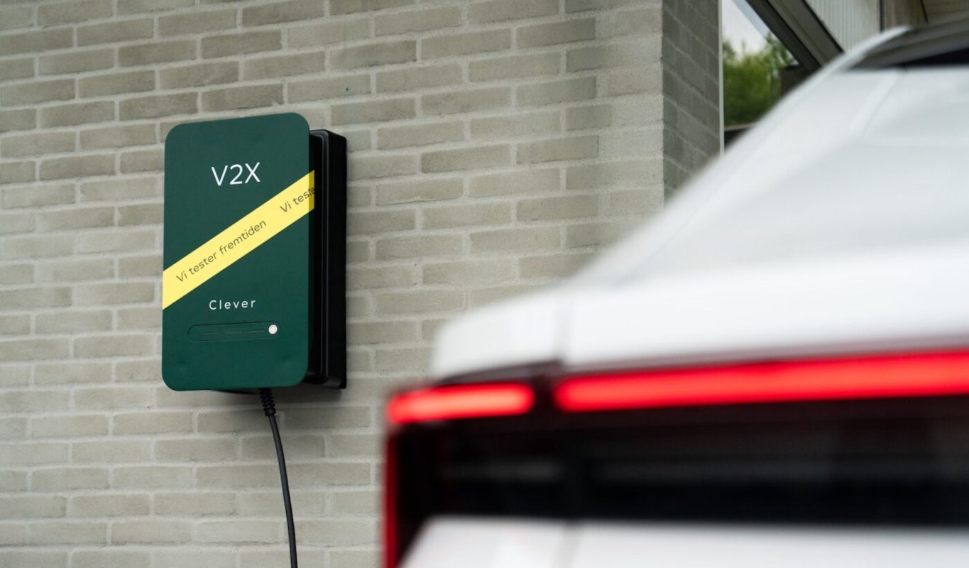 A green wall-mounted electric vehicle charger next to a white car.