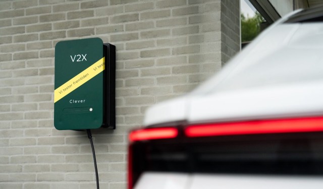 A green wall-mounted electric vehicle charger next to a white car.