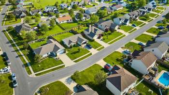 An aerial view of a suburban neighborhood with houses, green lawns, and winding streets.