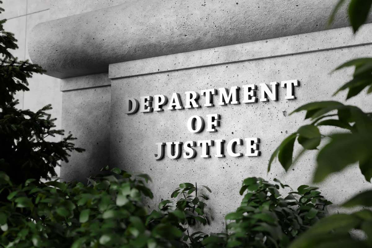 A close-up of a concrete wall with the words "DEPARTMENT OF JUSTICE" prominently displayed amid green foliage.