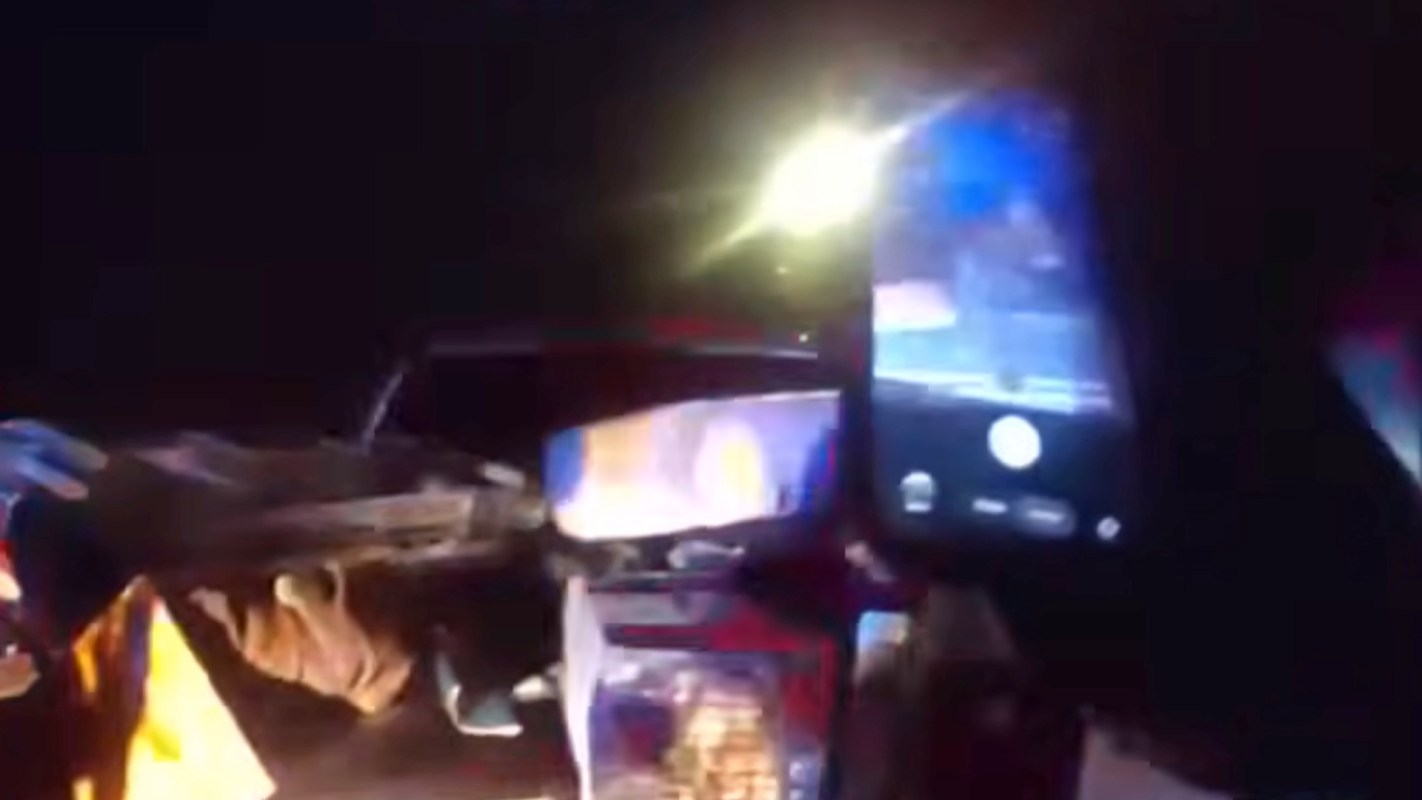 A close-up view of a hand holding a smartphone filming the back of a pickup truck, with bright lights in the background.