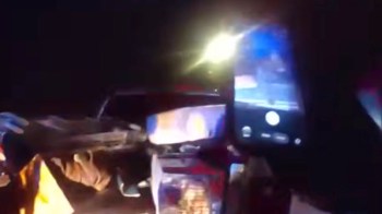 A close-up view of a hand holding a smartphone filming the back of a pickup truck, with bright lights in the background.