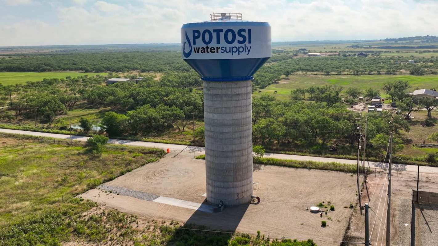 A tall water tower labeled "Potosi Water Supply" surrounded by green fields and a rural road.