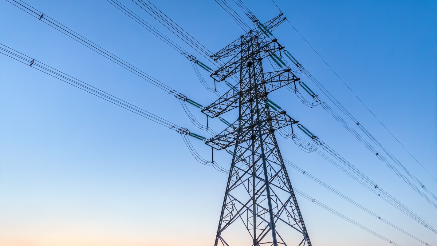 A high-voltage power line tower silhouetted against a clear blue sky.
