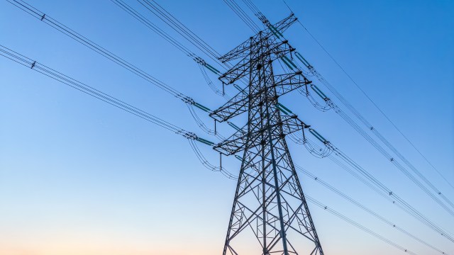 A high-voltage power line tower silhouetted against a clear blue sky.