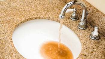 Brown water pours from a faucet into a white sink.