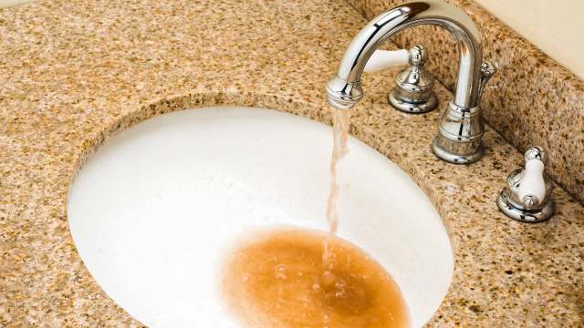 Brown water pours from a faucet into a white sink.