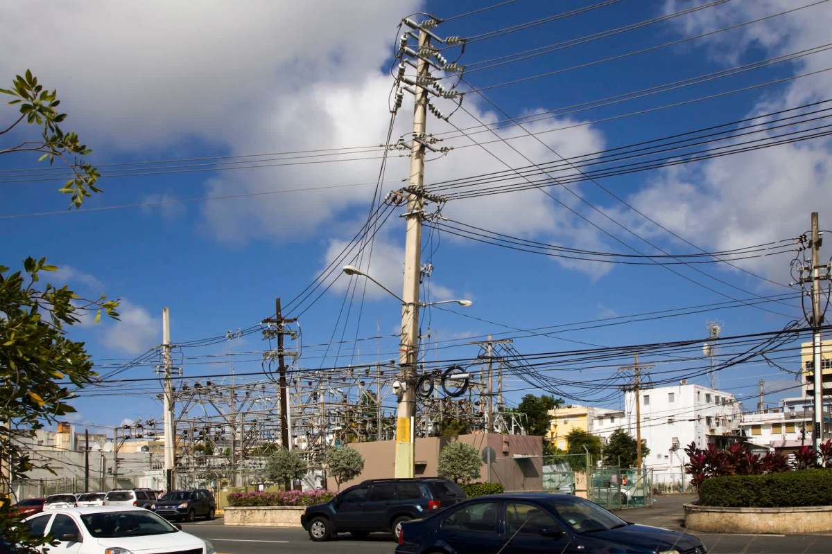 A busy urban scene featuring utility poles, power lines, and nearby vehicles under a blue sky with scattered clouds.