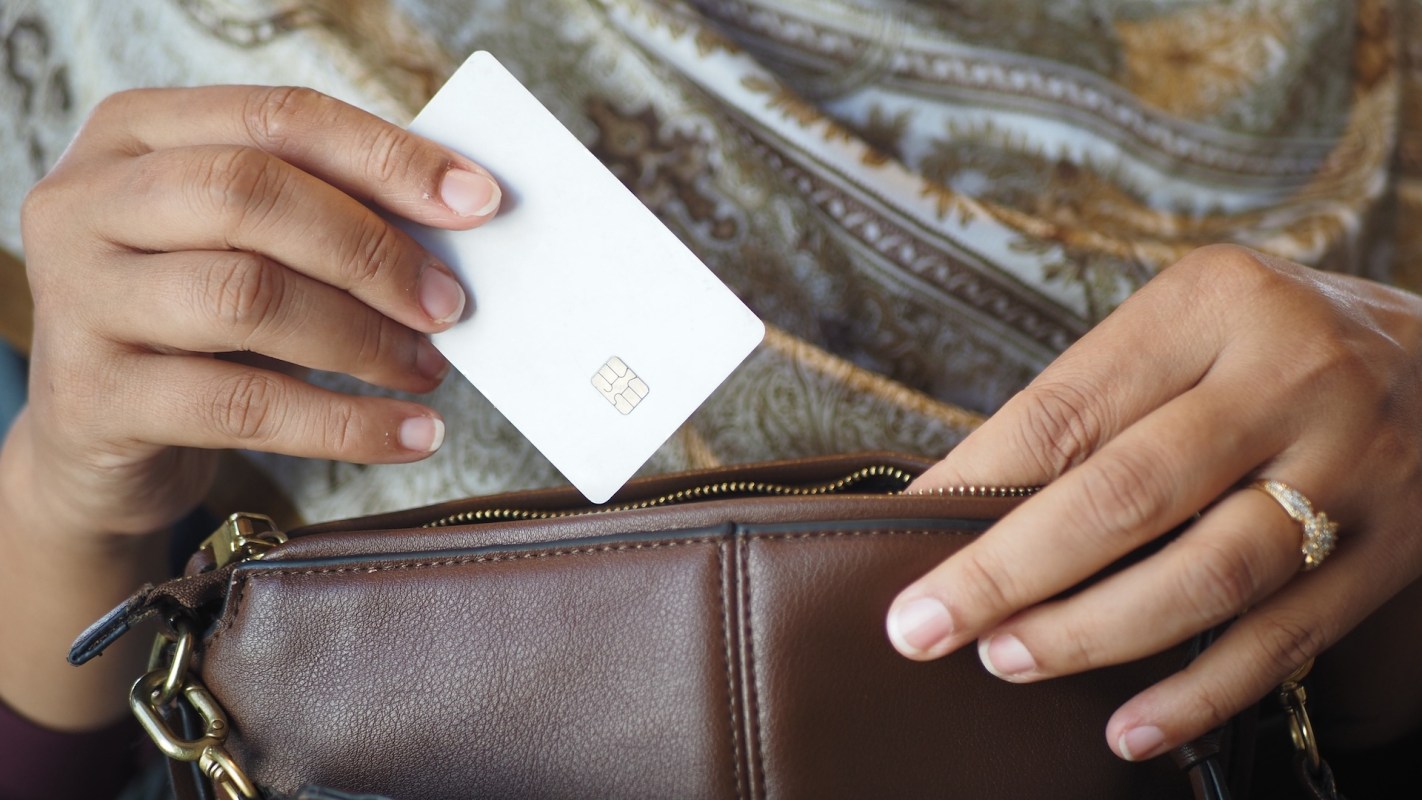 A person holding a white card above a brown handbag while wearing a decorative garment.