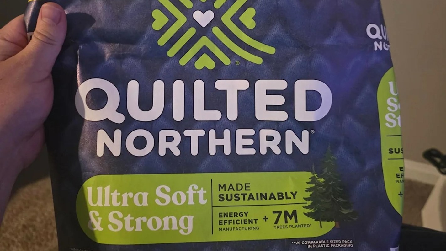 A person holds a package of Quilted Northern toilet paper, labeled "Ultra Soft & Strong" and featuring sustainability claims.