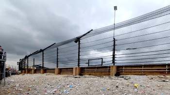 A raceway fence overlooking a litter-strewn area under a cloudy sky, with spectators visible in the background.