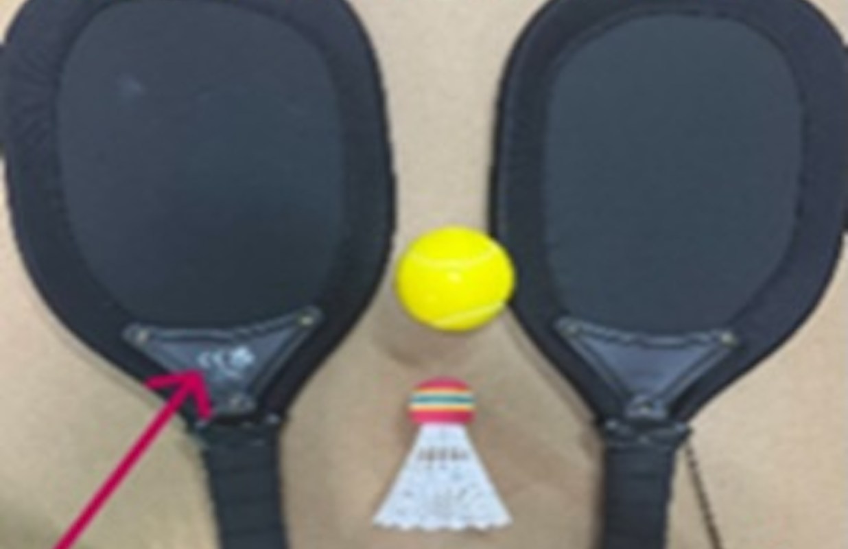 Two black paddles, a yellow ball, and a shuttlecock arranged on a light brown surface.