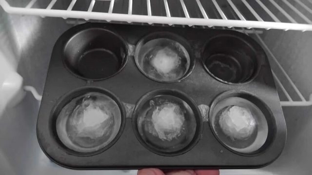A close-up of two muffin trays with brown paper liners in one tray on a dark countertop.