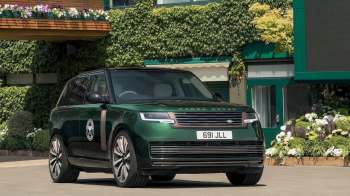 A green Range Rover SUV parked in front of a building covered in ivy and flower planters.