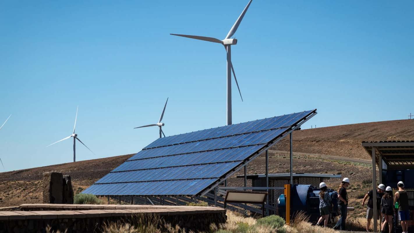 A solar panel array in front of wind turbines.