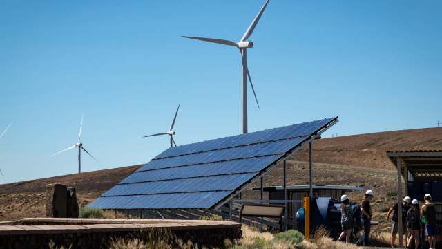 A solar panel array in front of wind turbines.