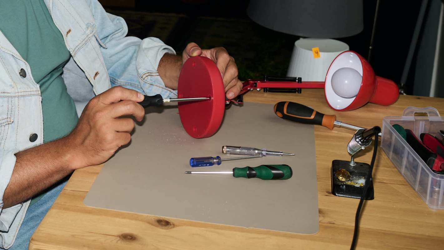 A person uses a screwdriver to assemble a red circular object on a work surface filled with tools.