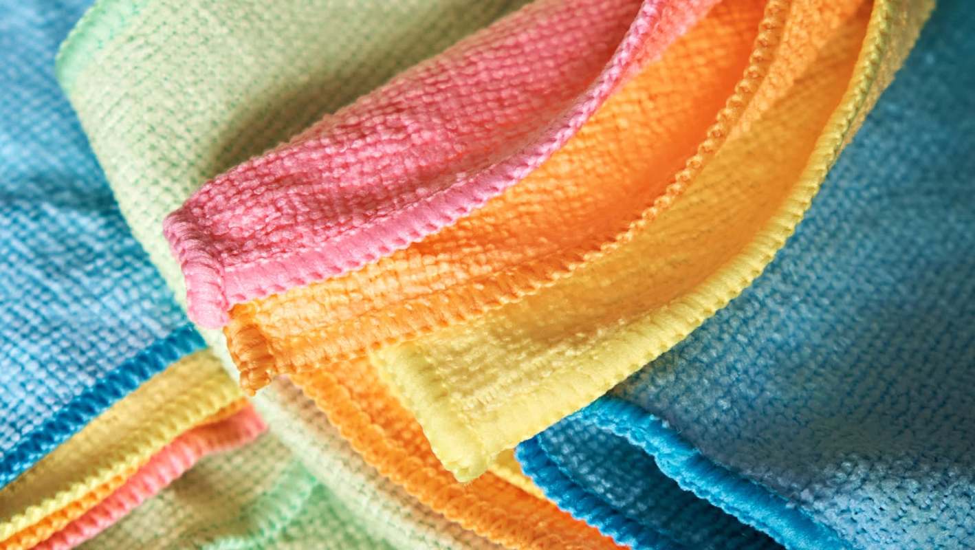 A close-up of colorful microfiber cloths in shades of pink, orange, yellow, green, and blue stacked together.